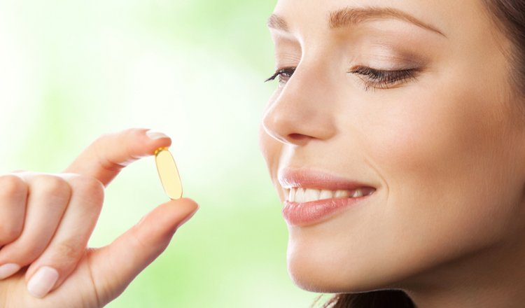 Young smiling woman with Omega 3 fish oil capsule, outdoor height=