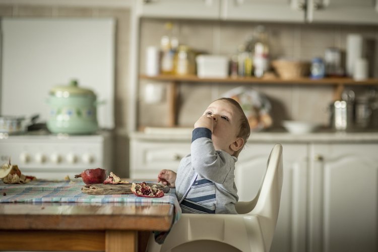 Portrait of happy baby boy in high chair and eating pomegranate