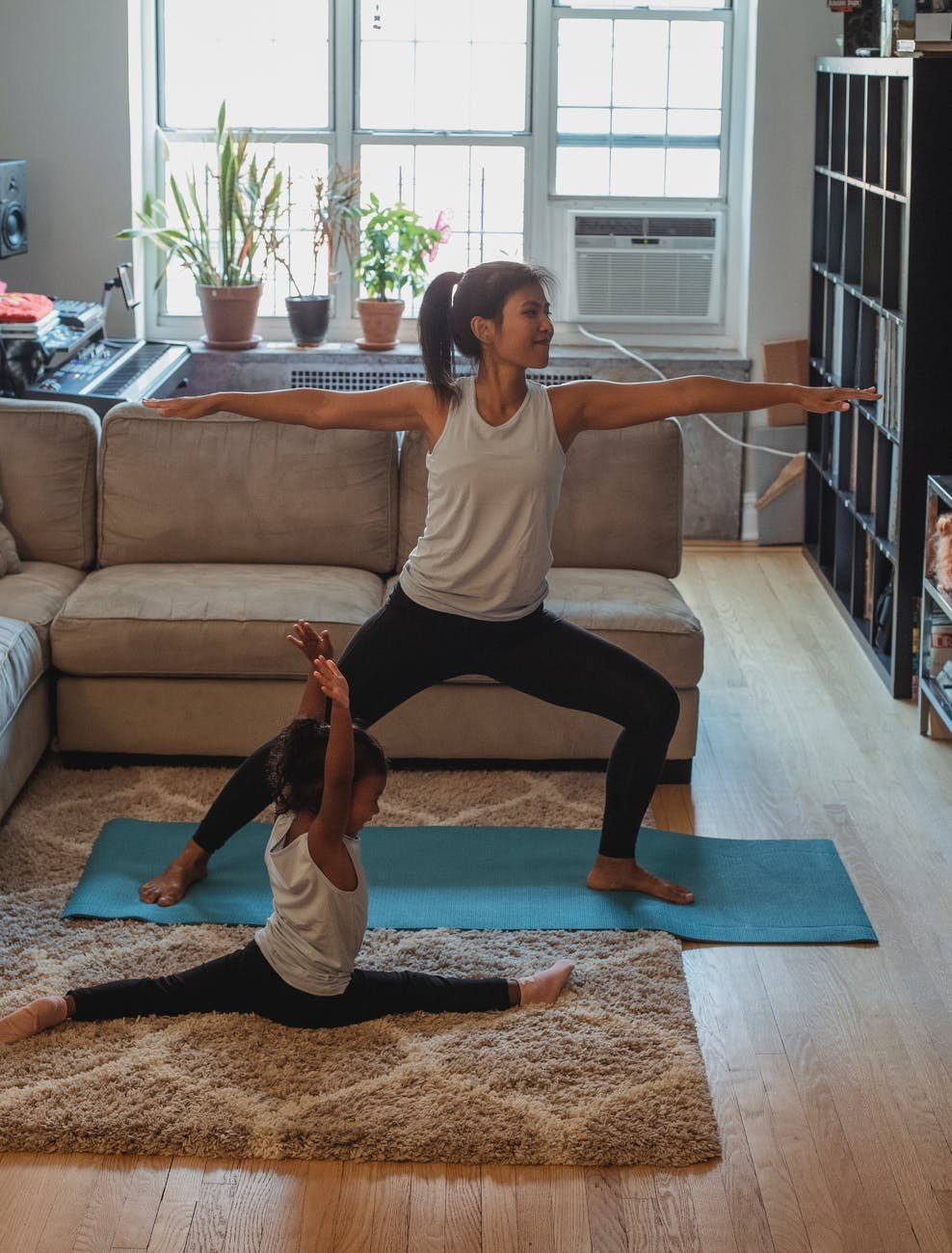 young ethnic woman performing warrior pose near daughter doing split