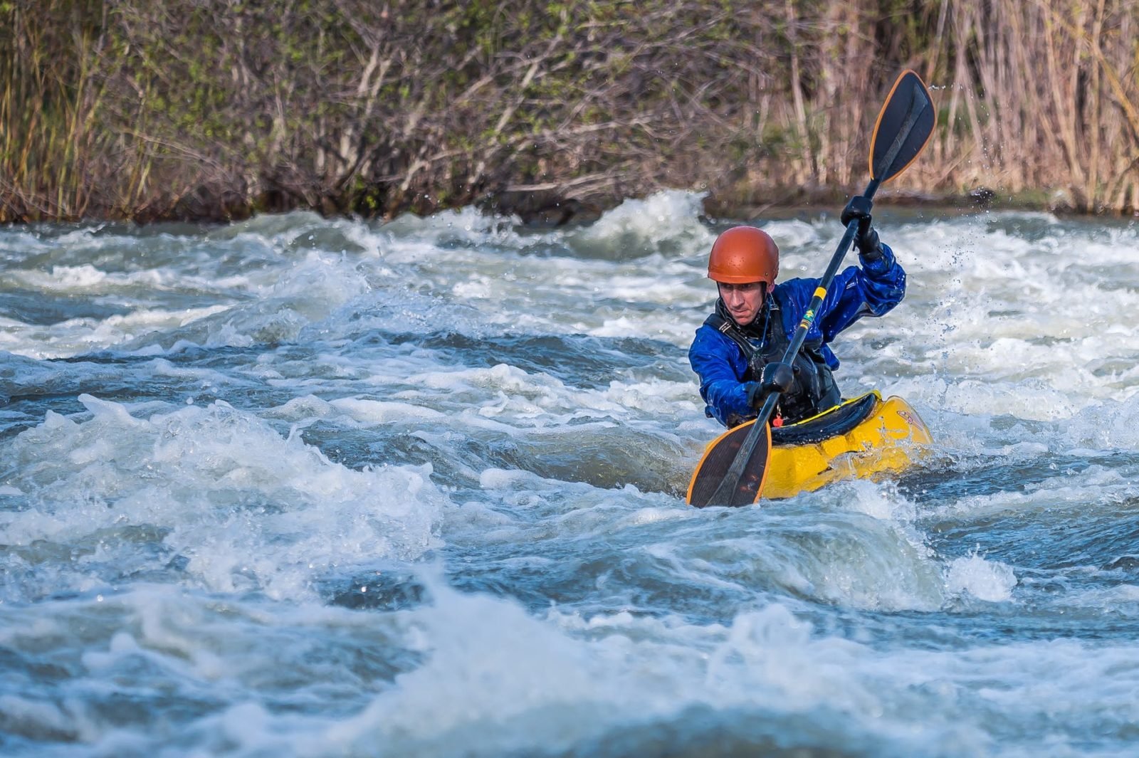 photo of man paddling kayak in raging river