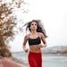 Determined woman in red leggings jogging along a scenic riverside path, embracing fitness outdoors.
