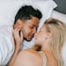 A loving couple, man and woman, resting closely together on a bed indoors during the daytime.