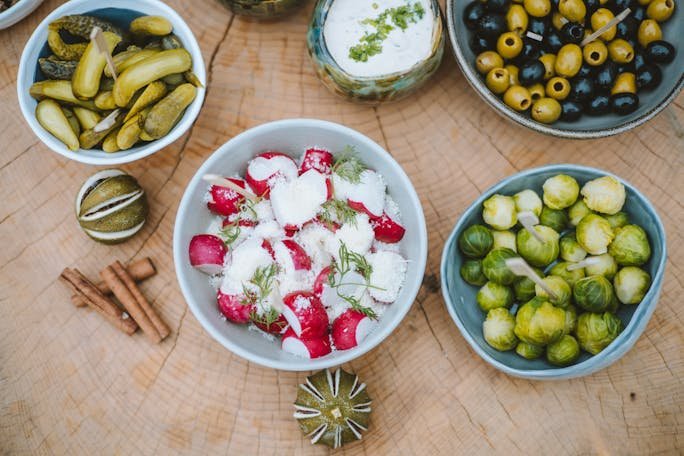 A vibrant assortment of vegetables, olives, and spices in bowls on a tree stump background.