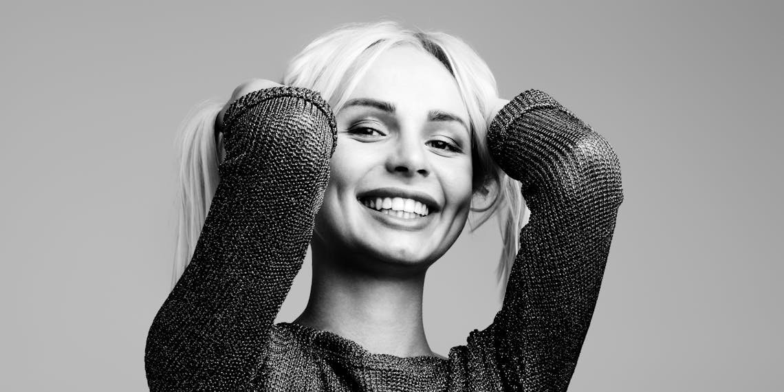 Black and white portrait of a woman smiling joyfully with hands in hair in a studio setting.