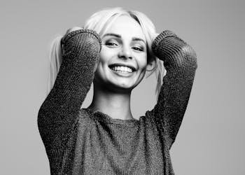 Black and white portrait of a woman smiling joyfully with hands in hair in a studio setting.