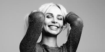 Black and white portrait of a woman smiling joyfully with hands in hair in a studio setting.