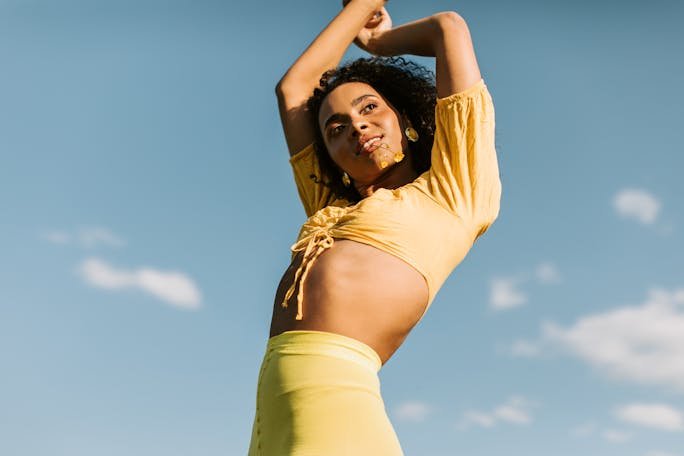 Charming woman with curly hair poses confidently against a clear blue sky, exuding joy and energy.
