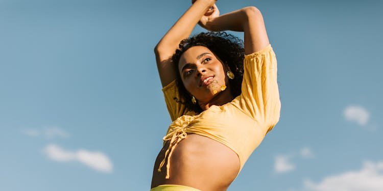 Charming woman with curly hair poses confidently against a clear blue sky, exuding joy and energy.