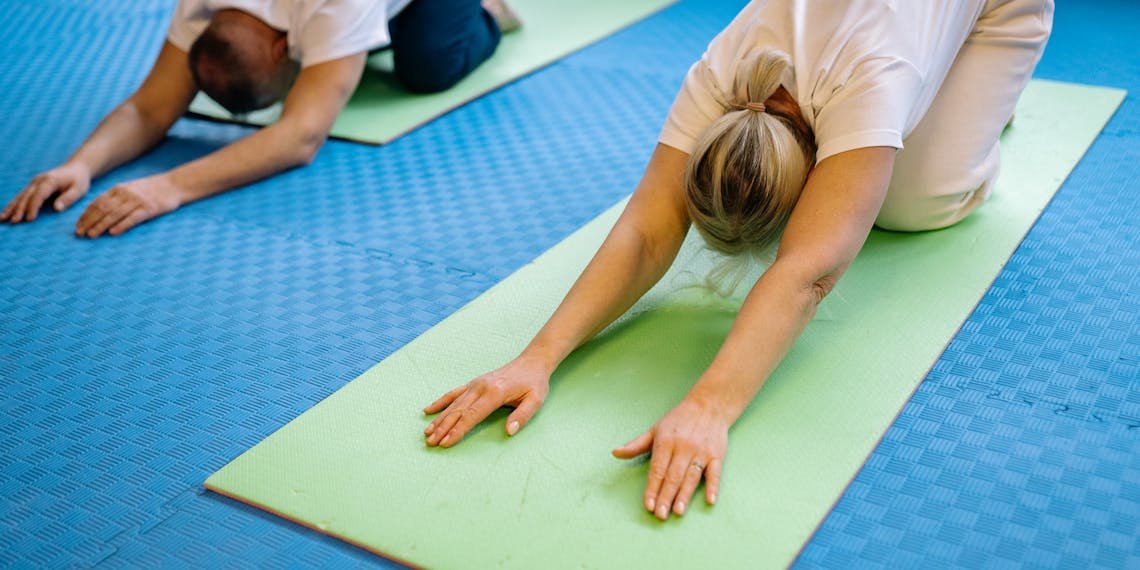 Senior adults stretching on yoga mats inside a gym, promoting health and fitness.