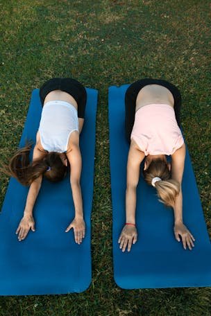 Two women performing yoga poses on mats outdoors, emphasizing fitness and tranquility.