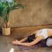 Woman in child's pose on yoga mat with candles and plant, creating a serene indoor setting.
