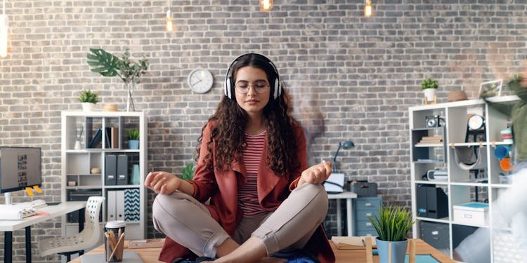 Young woman meditating with headphones in a modern office setting, practicing mindfulness.