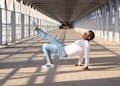 Man in casual wear showcases urban style with dynamic pose on sunlit bridge.