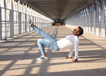 Man in casual wear showcases urban style with dynamic pose on sunlit bridge.