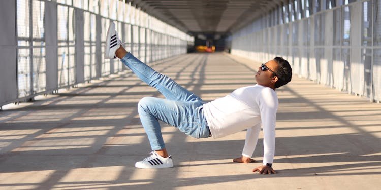 Man in casual wear showcases urban style with dynamic pose on sunlit bridge.