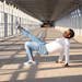 Man in casual wear showcases urban style with dynamic pose on sunlit bridge.