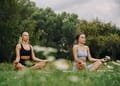 Two women practicing yoga meditation in a serene outdoor park setting.