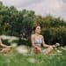Two women practicing yoga meditation in a serene outdoor park setting.